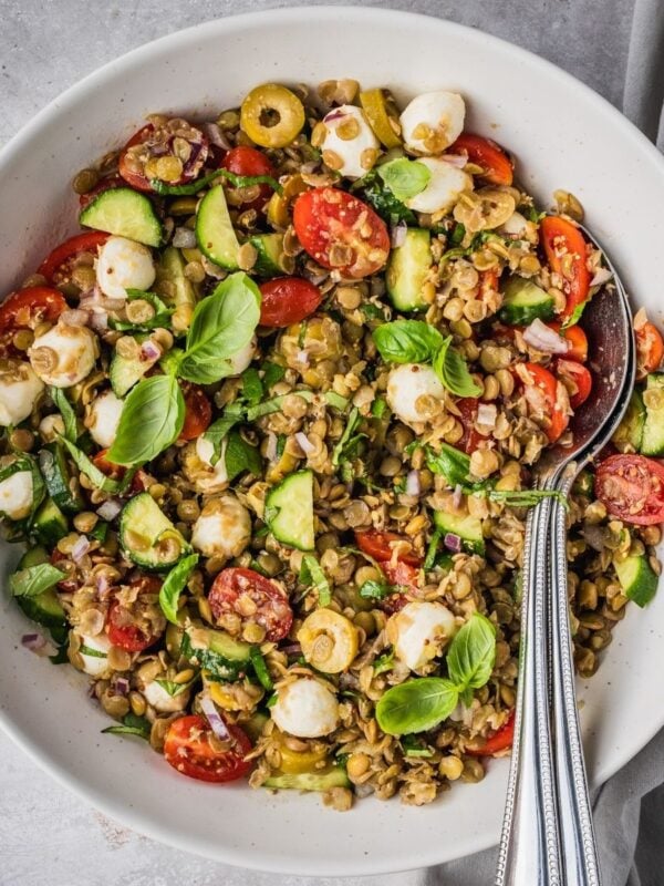 Mediterranean Lentil Salad with cooked green lentils, cherry tomatoes, cucumbers, mozzarella balls and fresh basil in a large serving bowl.