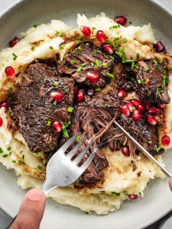 Bowl with mashed potatoes and pomegranate short ribs, garnished with chives and pomegranate seeds.