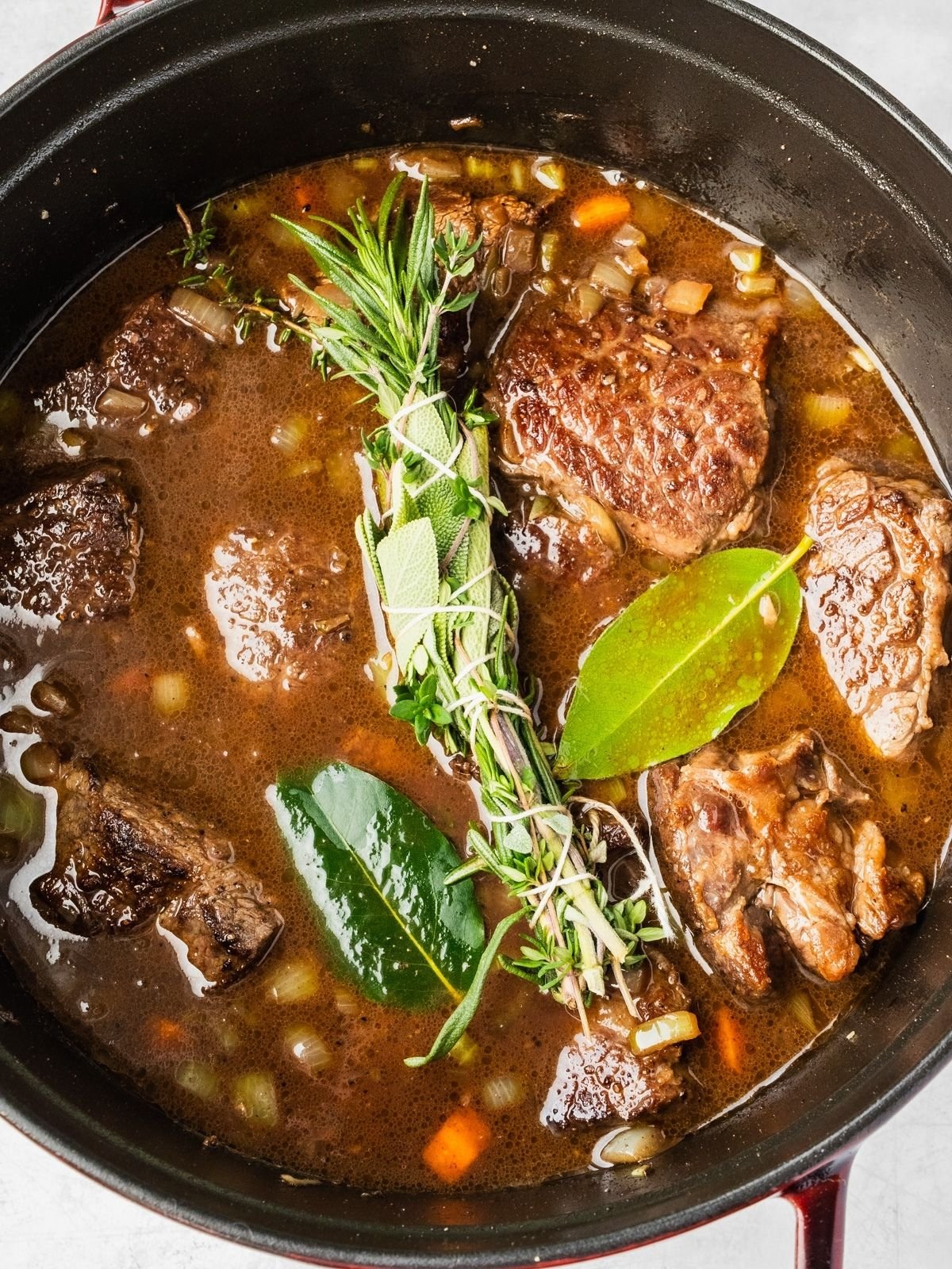 Large pot with the aromatics, broth, wine, seared beef and herbs.