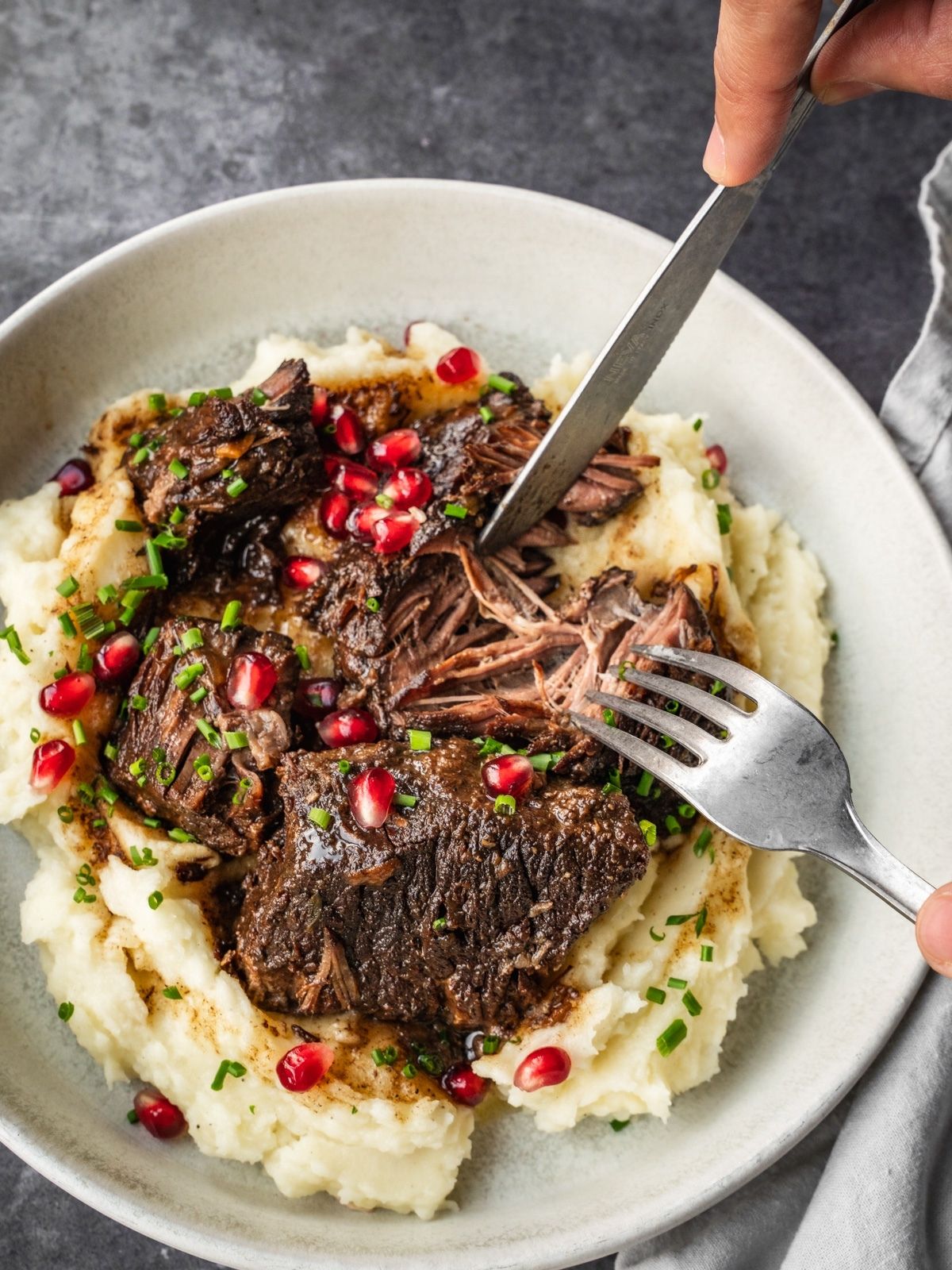 Bowl with mashed potatoes and braised pomegranate short ribs, garnished with chives and fresh pomegranate seeds.