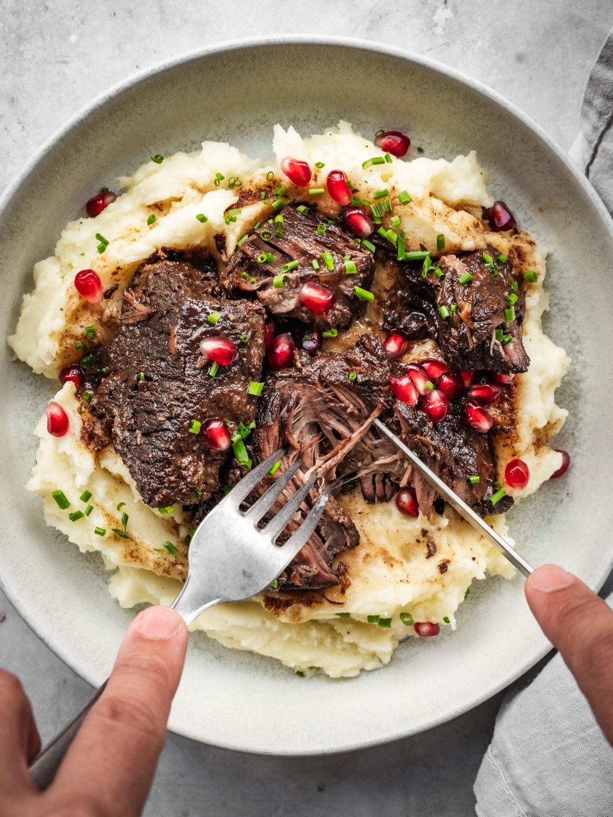 Bowl with mashed potatoes and braised pomegranate short ribs, garnished with chives and fresh pomegranate seeds.