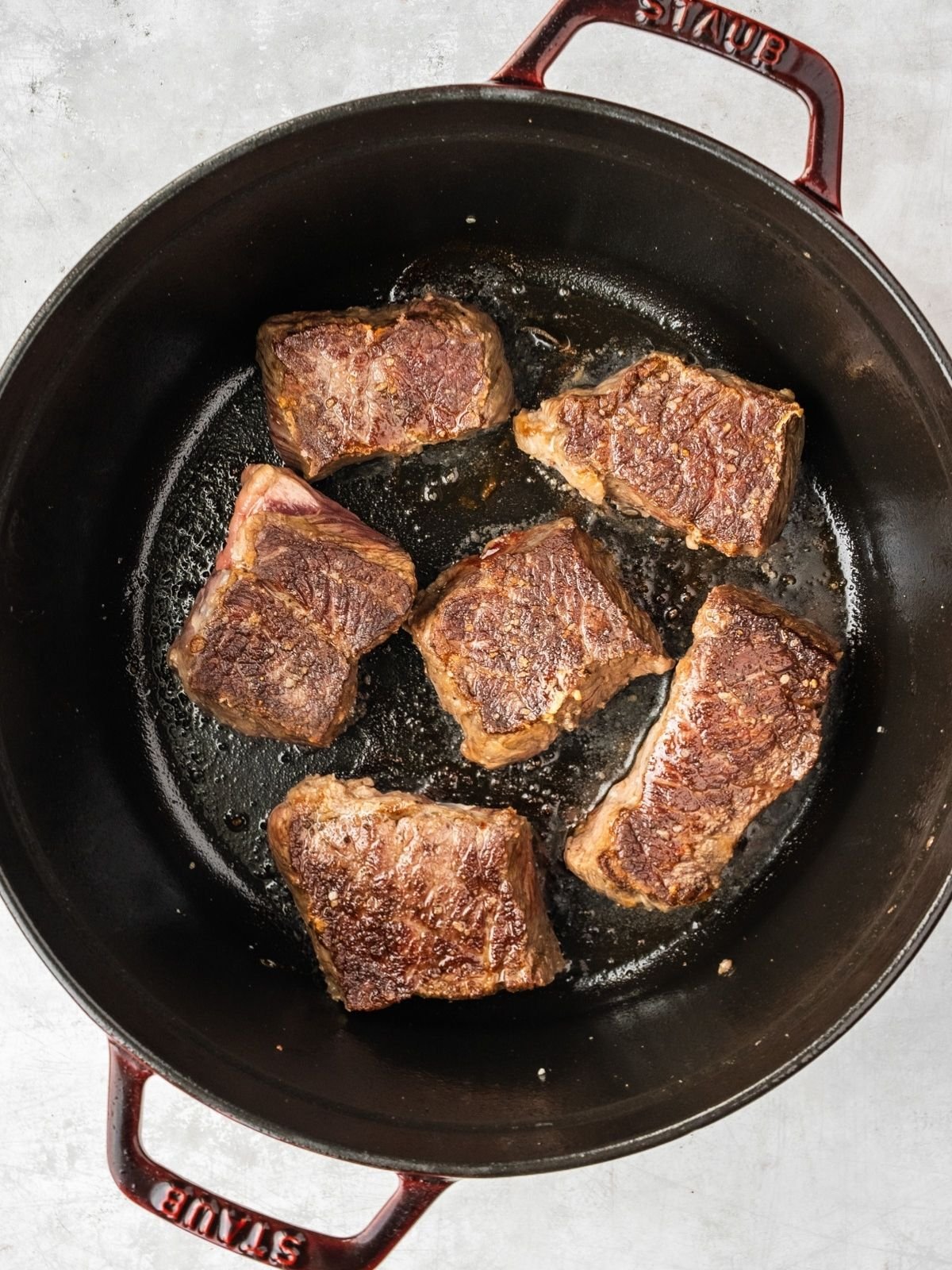 6 large beef short rib chunks are getting seared in a large cast iron pot.