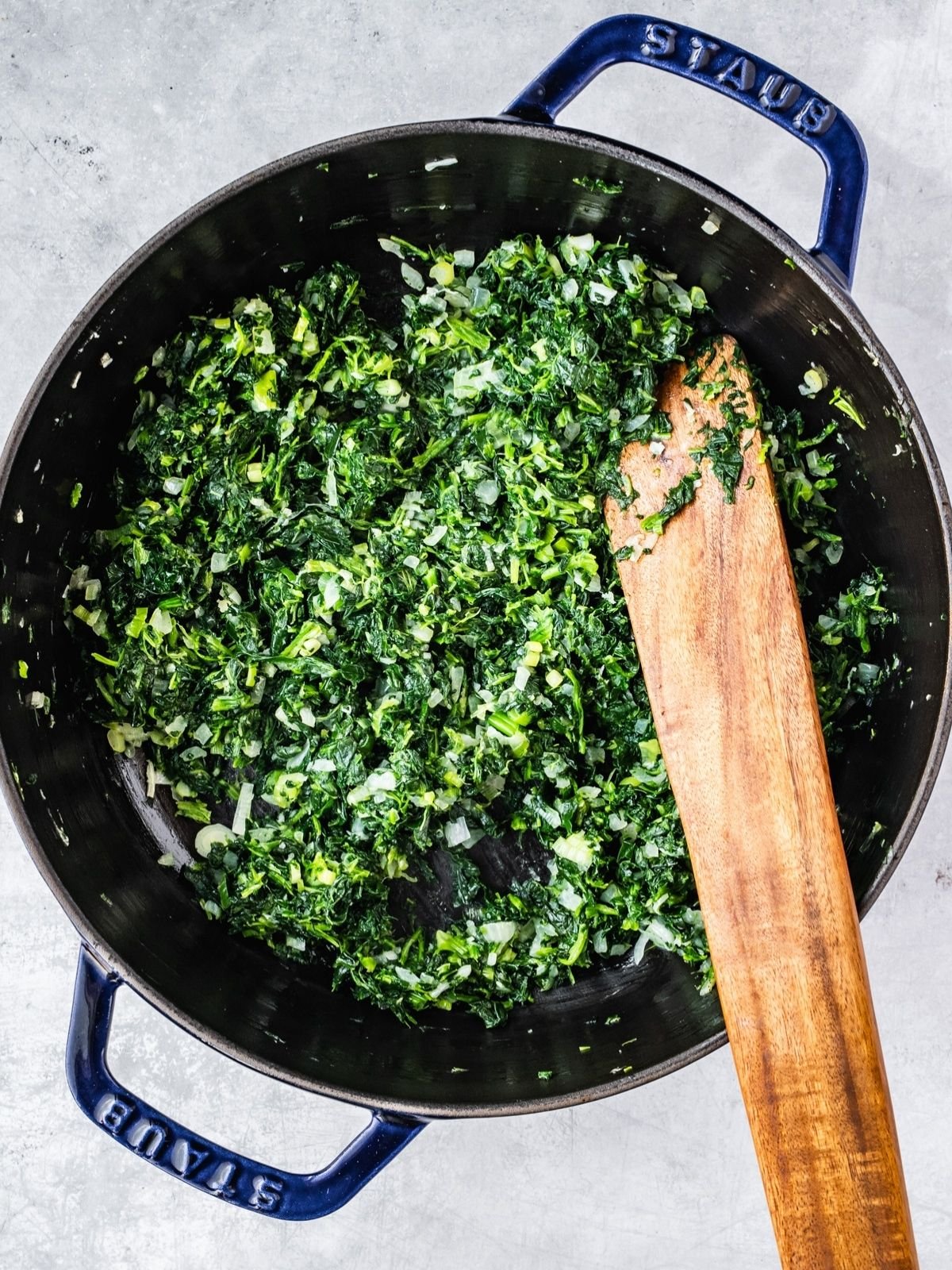 Adding the frozen and drained spinach to the pot with the fried onion.