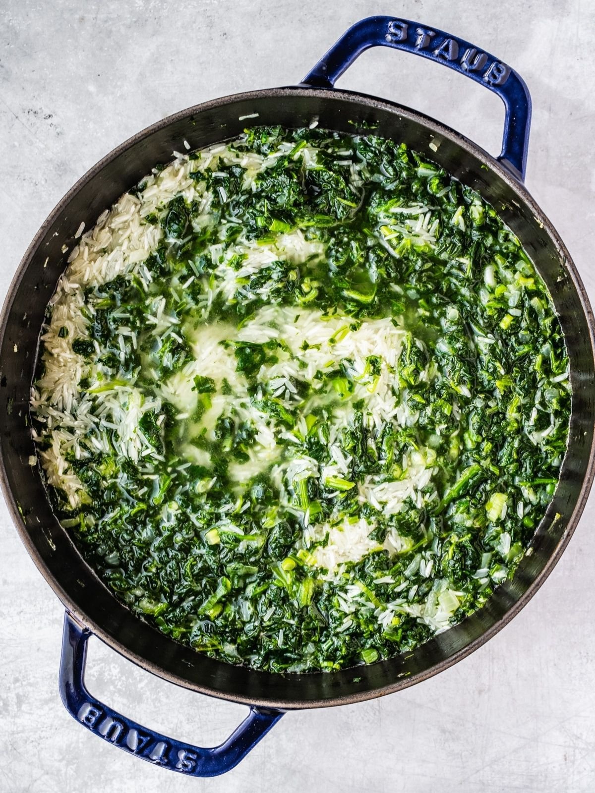 Adding the rice and water to the pot with the fried spinach and onion mixture.