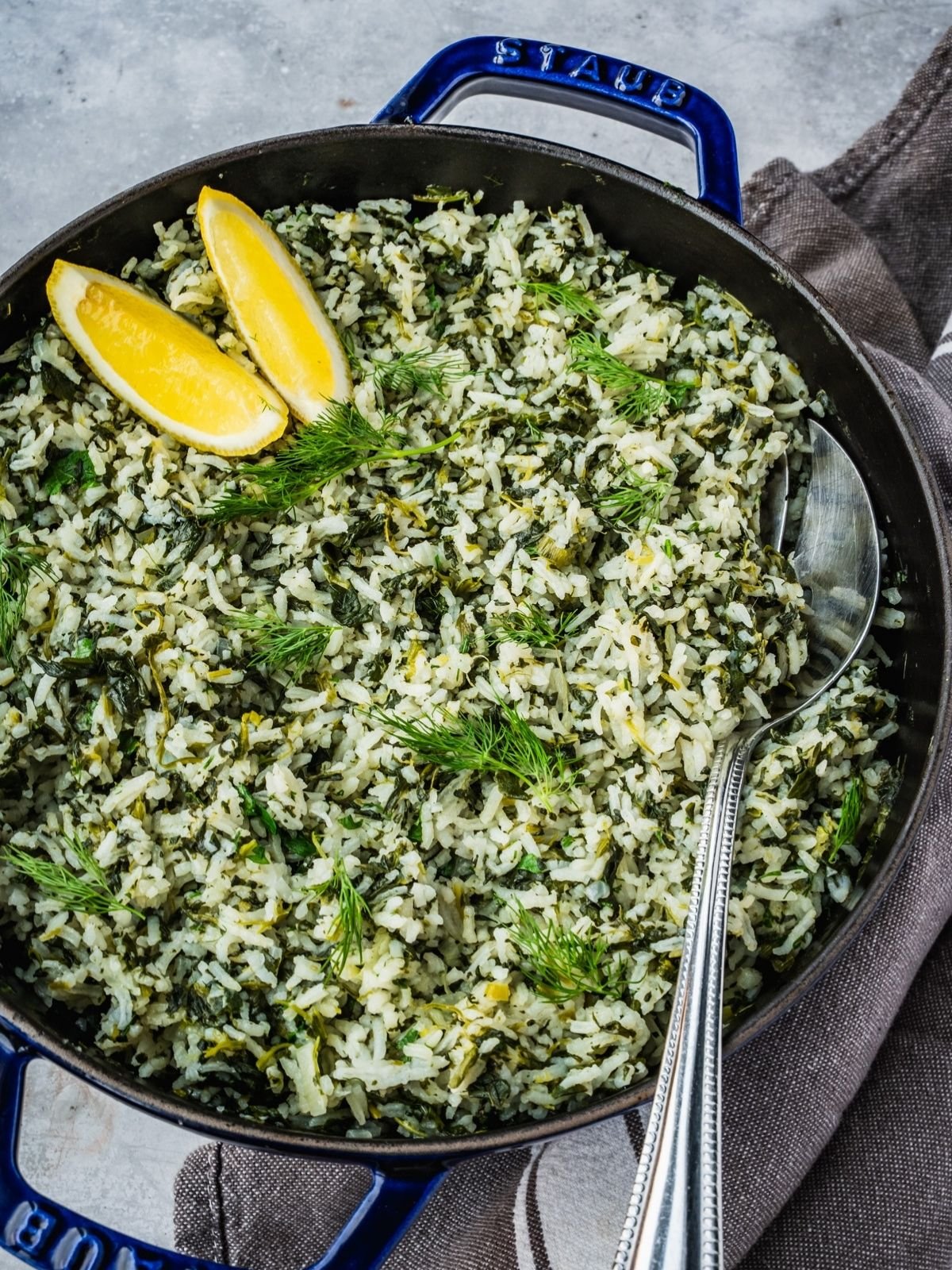 Spanakorizo Greek Rice with spinach in a large pot, garnished with lemon wedges and extra fresh dill.