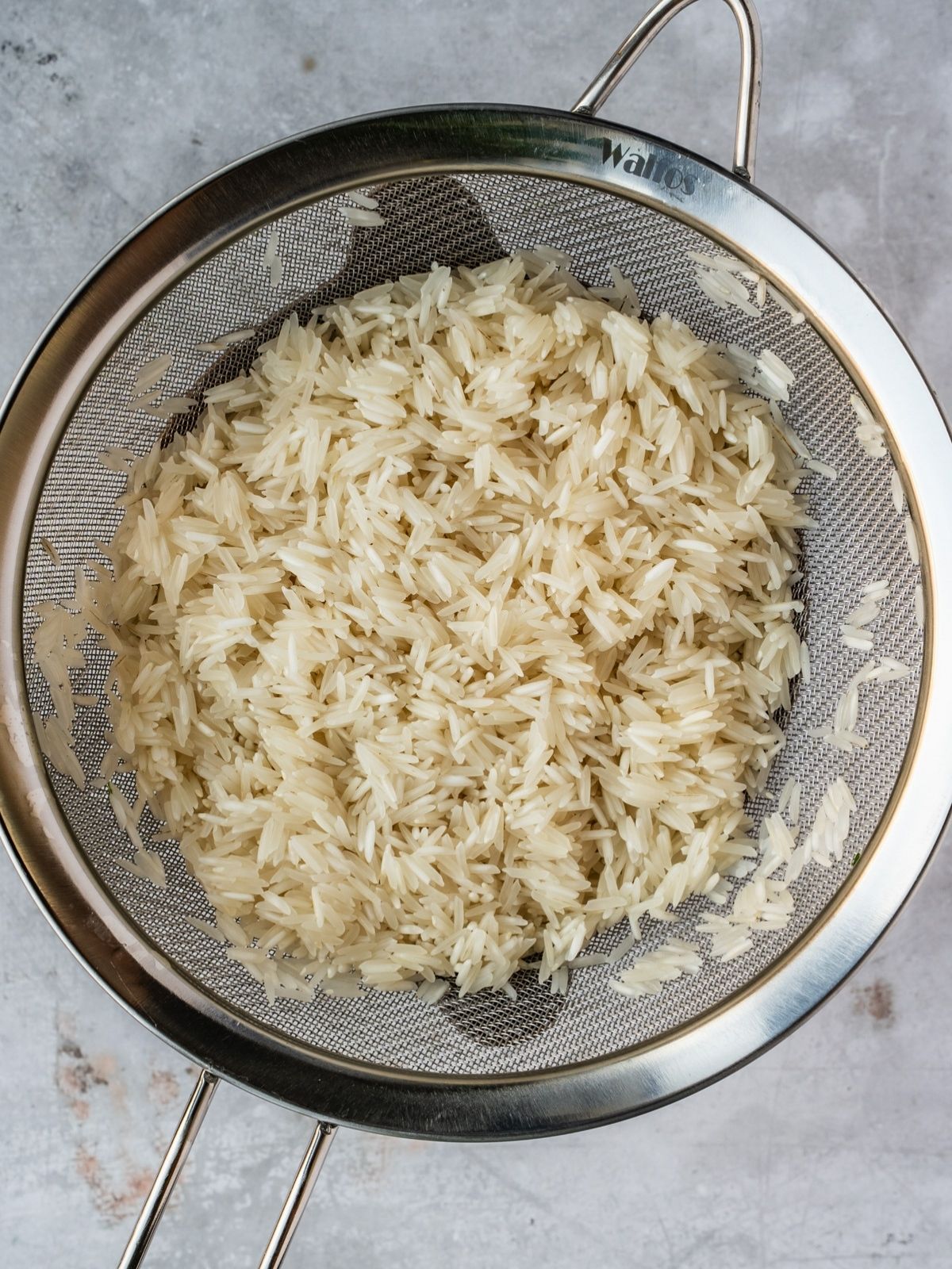 Rinsed rice draining in a small metal sieve.