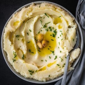 Bowl of garlic confit mashed potatoes garnished with extra confit garlic and chives.