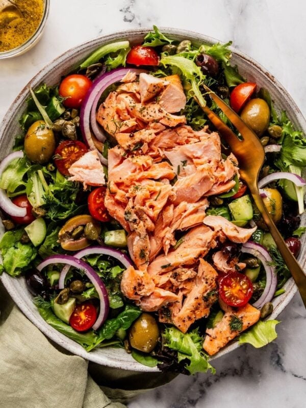 Mediterranean Salmon Salad bowl with flaky salmon over a bed of greens, tomatoes, olives and cucumbers.
