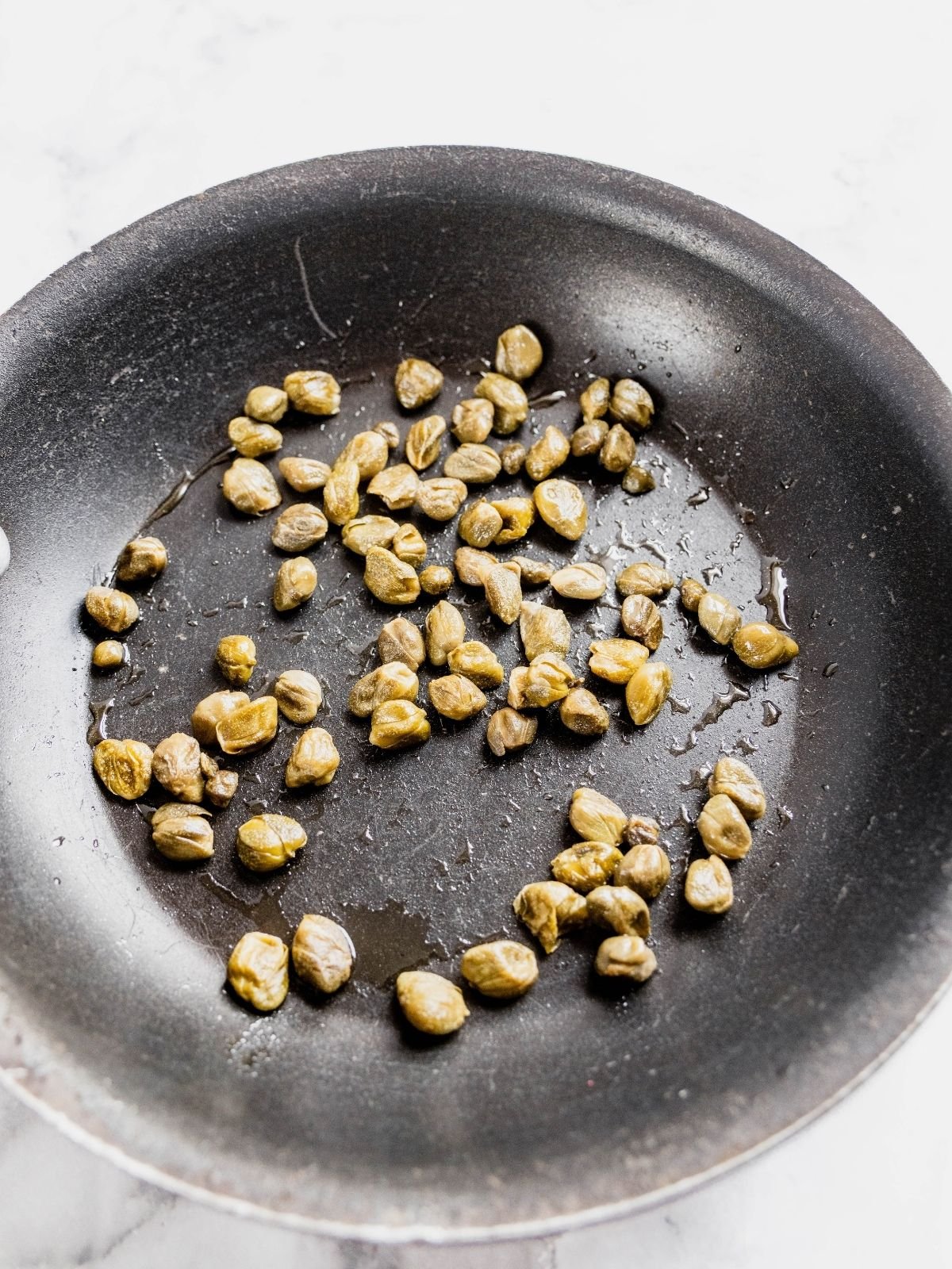 Capers frying in a small frying pan.
