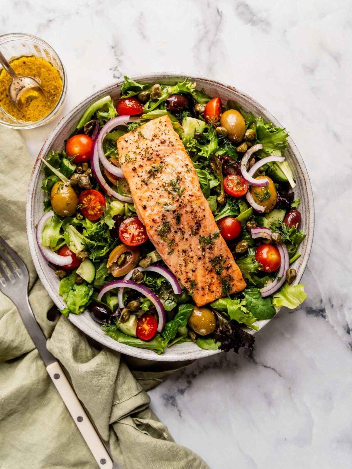 Mediterranean Salmon Salad bowl with flaky salmon over a bed of greens, tomatoes, olives and cucumbers.