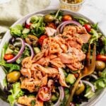 Mediterranean Salmon Salad bowl with flaky salmon over a bed of greens, tomatoes, olives and cucumbers.