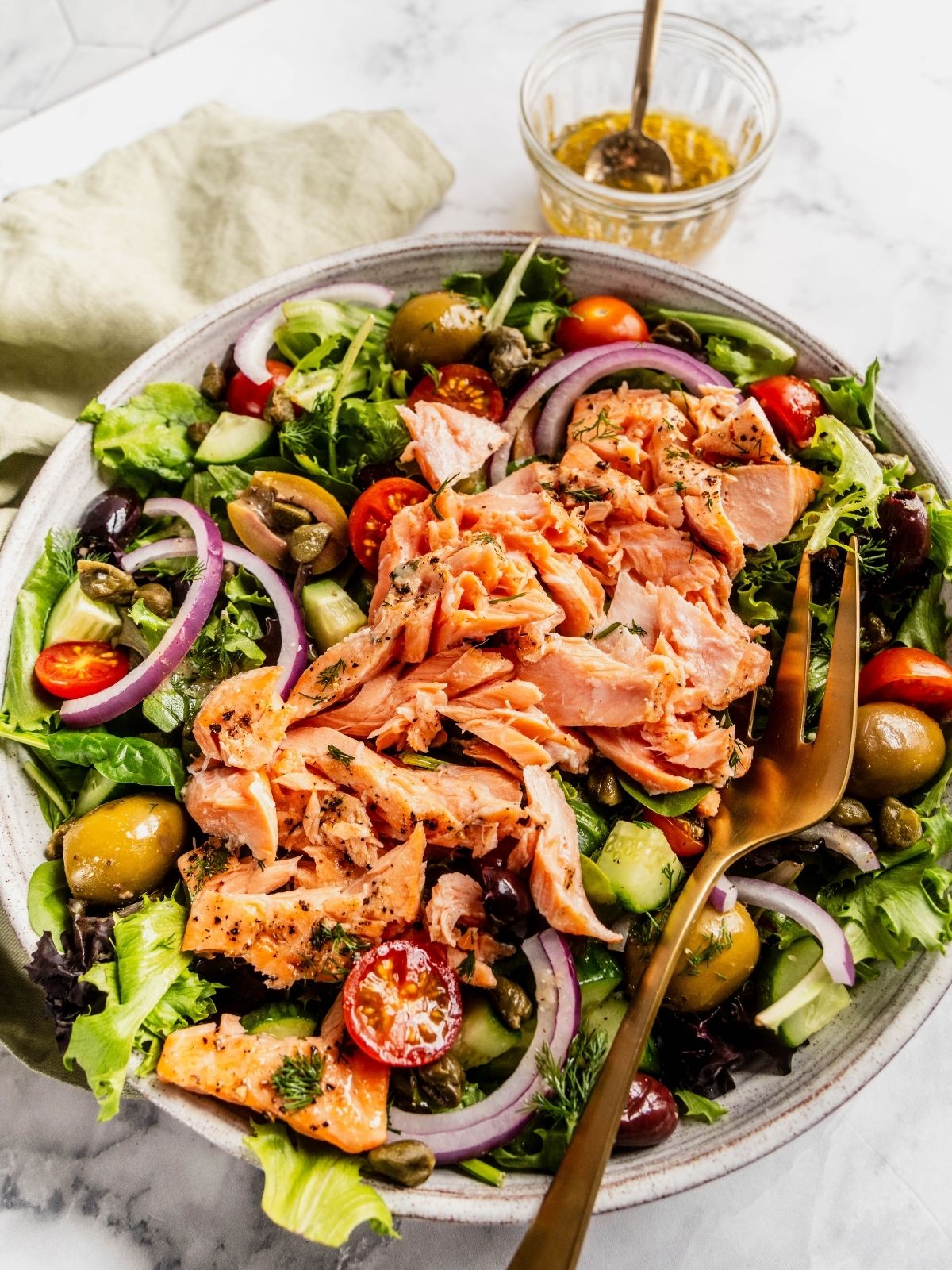 Mediterranean Salmon Salad bowl with flaky salmon over a bed of greens, tomatoes, olives and cucumbers.