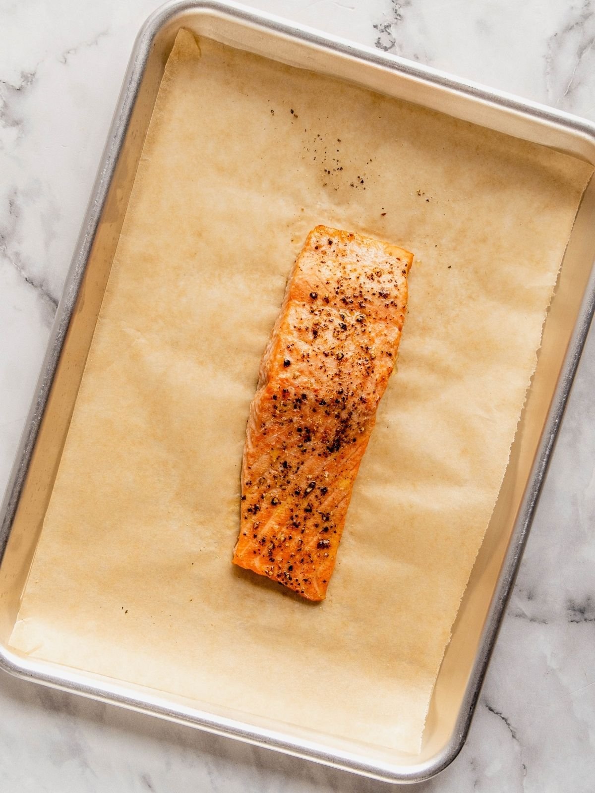 A cooked salmon filet on a parchment paper-lined baking sheet.