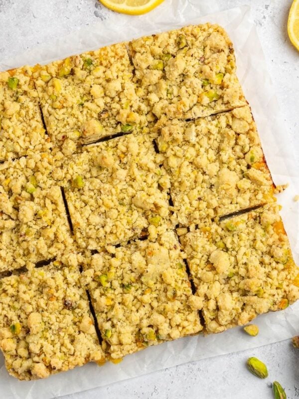 Sliced pistachio lemon bars on parchment paper with whole pistachios on the side.