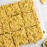 Sliced pistachio lemon bars on parchment paper with whole pistachios on the side.