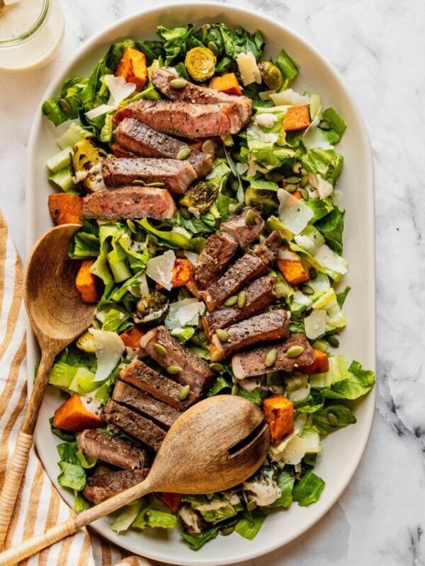 Steak Caesar Salad on a large serving platter garnished with parmesan shavings and pumpkin seeds.