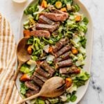 Steak Caesar Salad on a large serving platter garnished with parmesan shavings and pumpkin seeds.