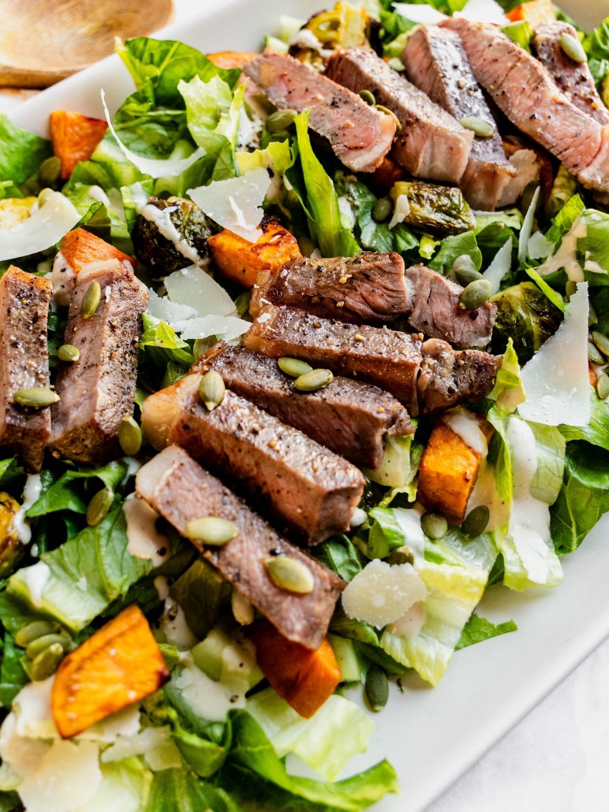 Steak Caesar Salad on a large serving platter garnished with parmesan shavings and pumpkin seeds.