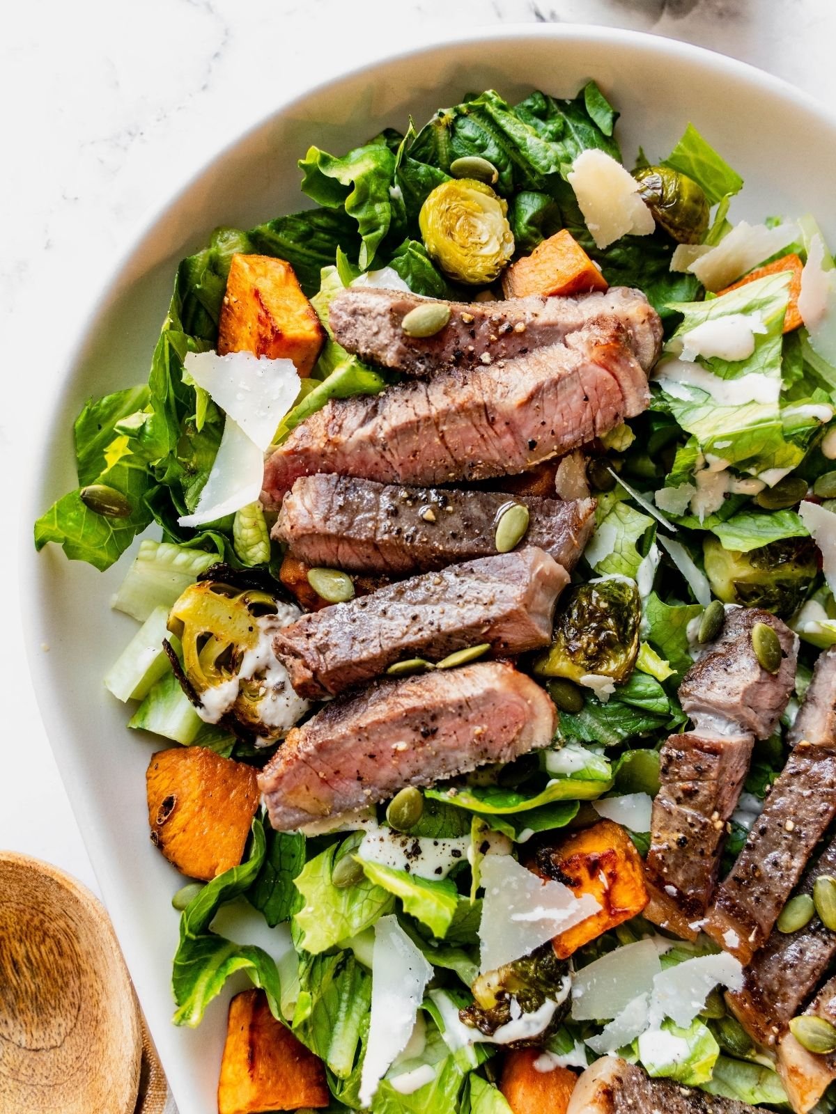 Steak Caesar Salad on a large serving platter garnished with parmesan shavings and pumpkin seeds.