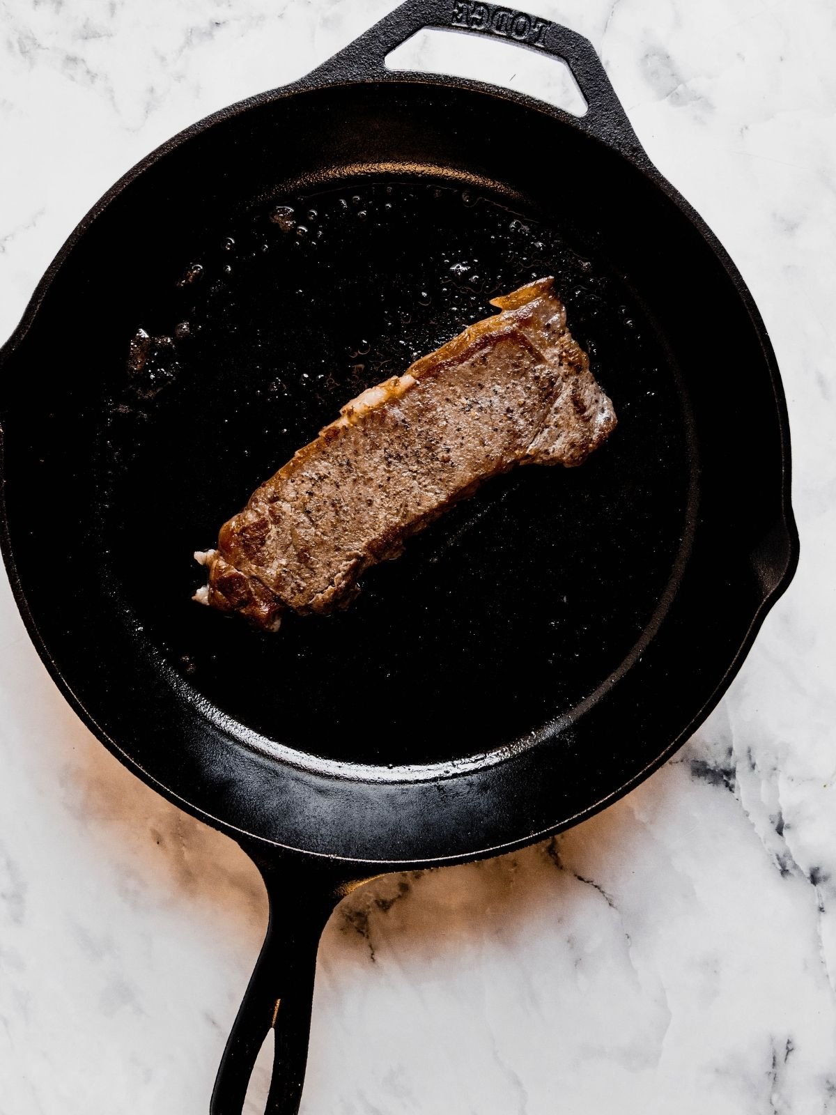 A New York Strip steak cooking in a cast iron pan.