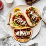 Plate with three turkey kofta wraps garnished with tahini sauce, pickled onions and chopped salad with cherry tomatoes and cucumbers.