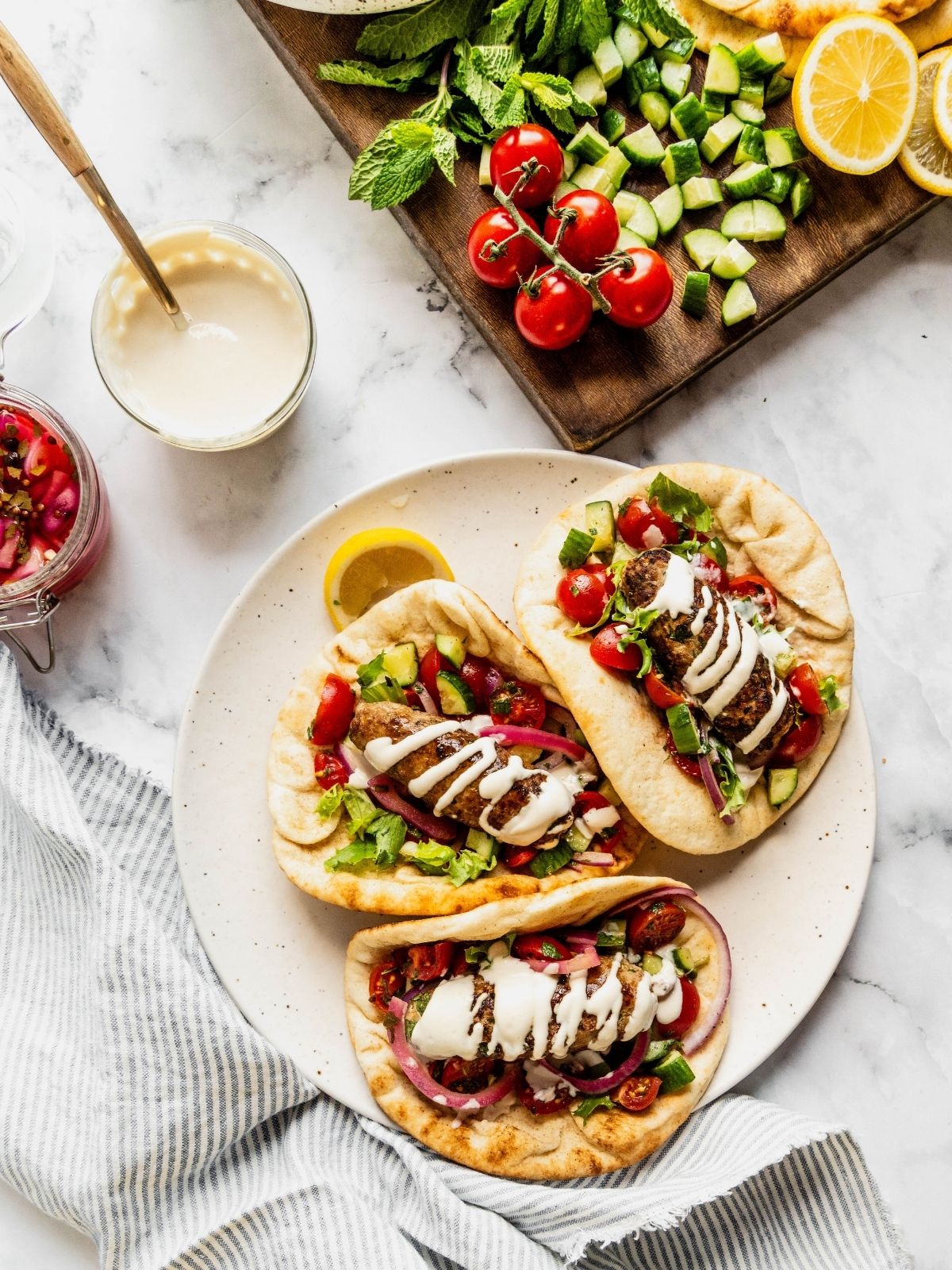 Plate with three turkey kofta wraps garnished with tahini sauce, pickled onions and chopped salad with cherry tomatoes and cucumbers.