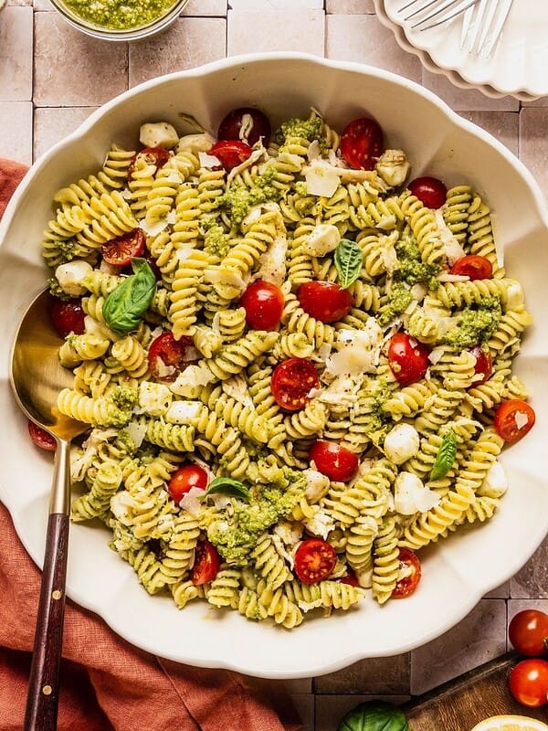 Chicken and pesto pasta salad in a large serving bowl garnished with basil leaves and shaved parmesan.