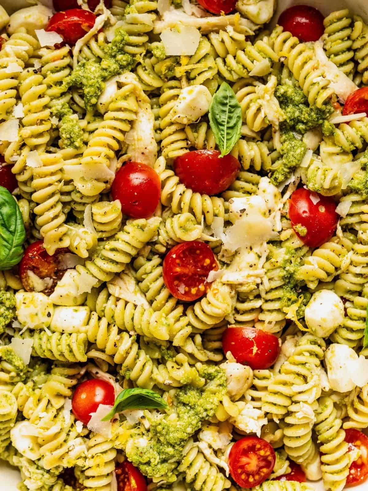 Chicken and pesto pasta salad garnished with basil leaves and shaved parmesan.