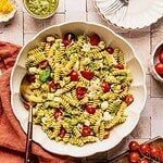 Chicken and pesto pasta salad in a large serving bowl garnished with basil leaves and shaved parmesan.