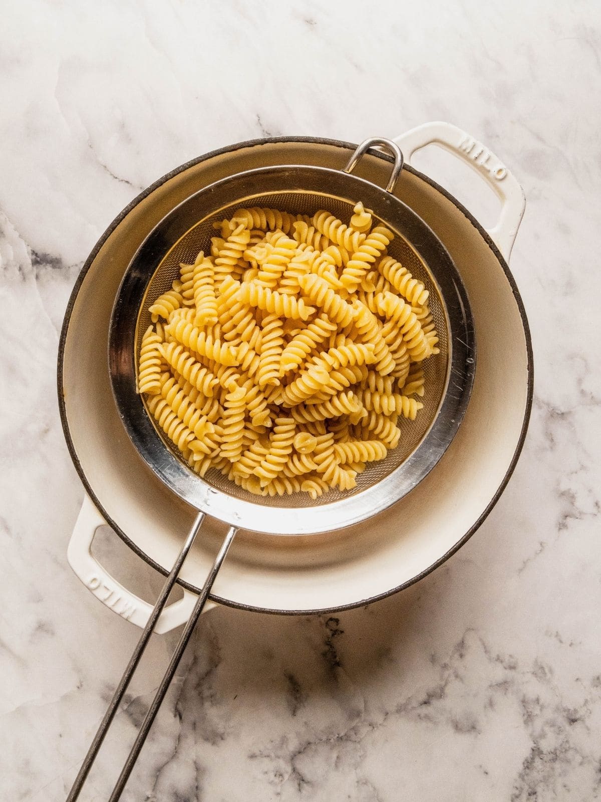 Cooked pasta draining in a sieve over a pot.
