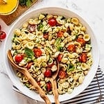 Mediterranean Chickpea Pasta Salad with cherry tomatoes and chopped cucumber in a large serving bowl with salad spoons.