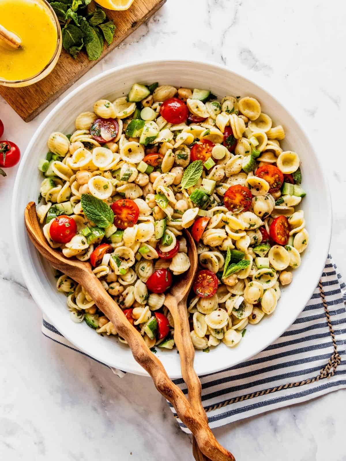 Mediterranean Chickpea Pasta Salad with cherry tomatoes and chopped cucumber in a large serving bowl with salad spoons.
