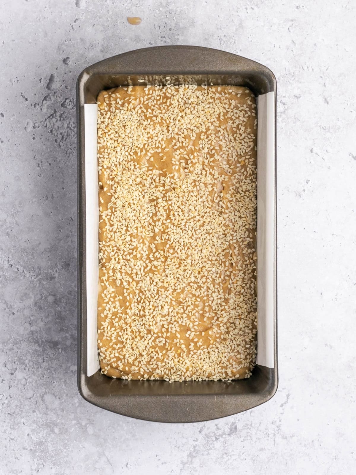 Parchment paper lined loaf pan with the banana bread batter, sprinkled with sesame seeds.