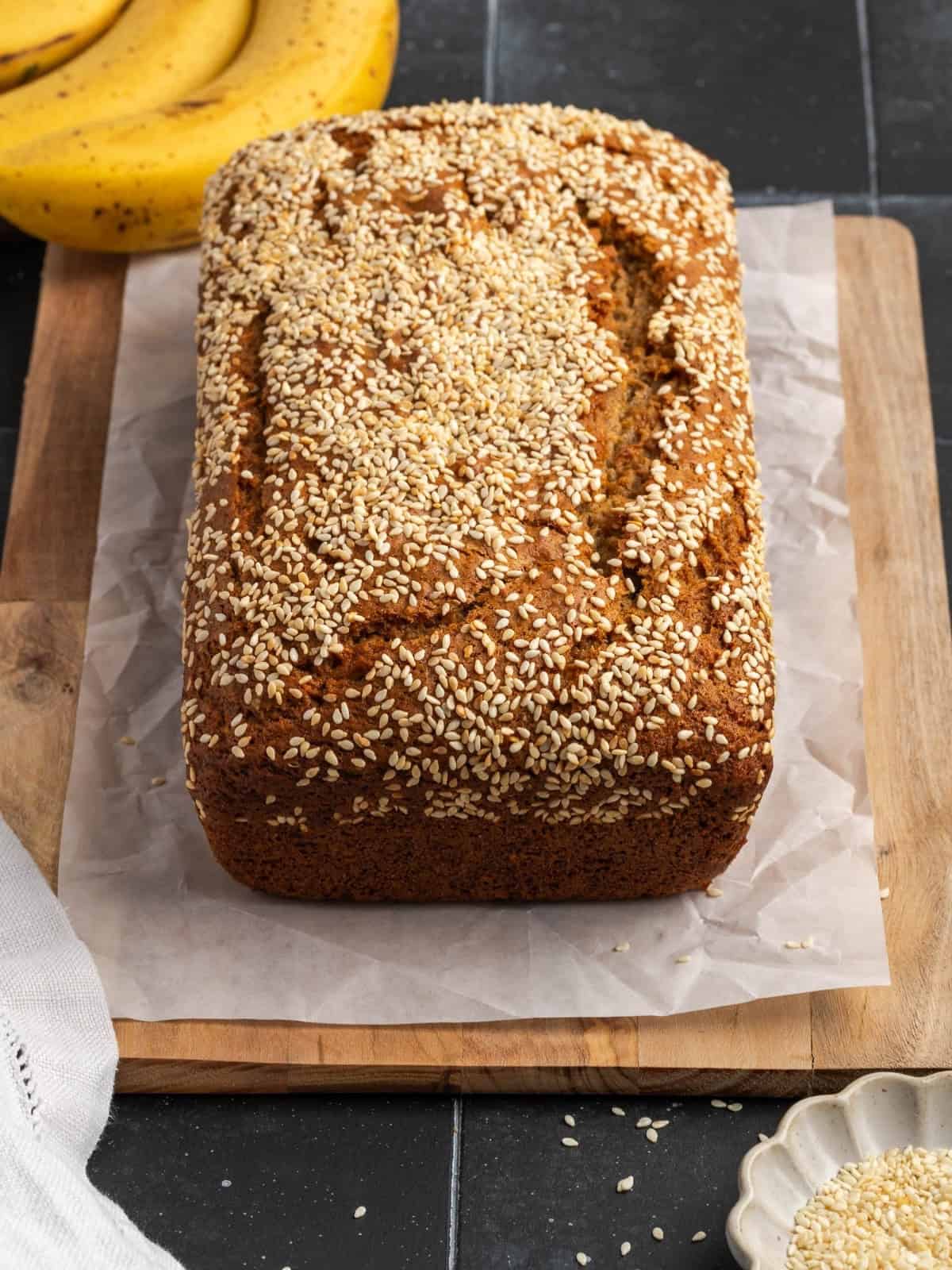Baked tahini banana bread on parchment paper sitting on top of a wooden cutting board.
