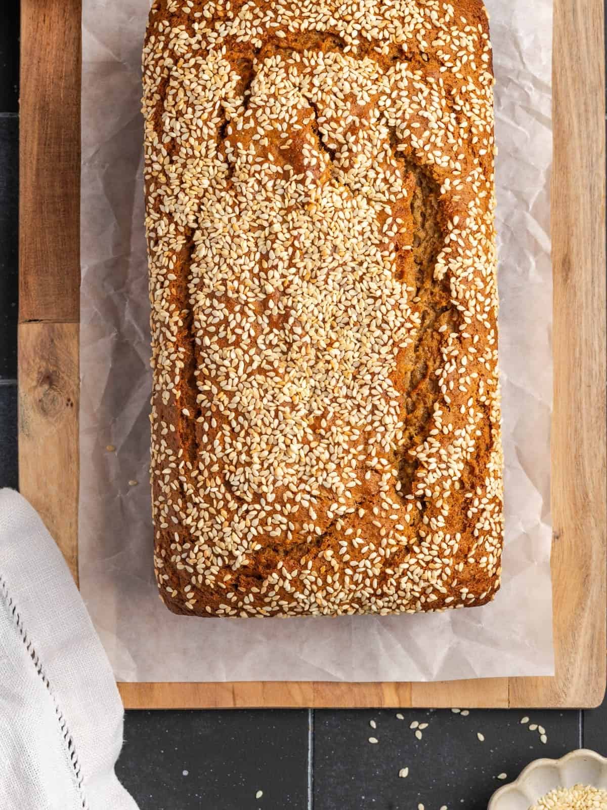 Baked tahini banana bread on parchment paper sitting on top of a wooden cutting board.
