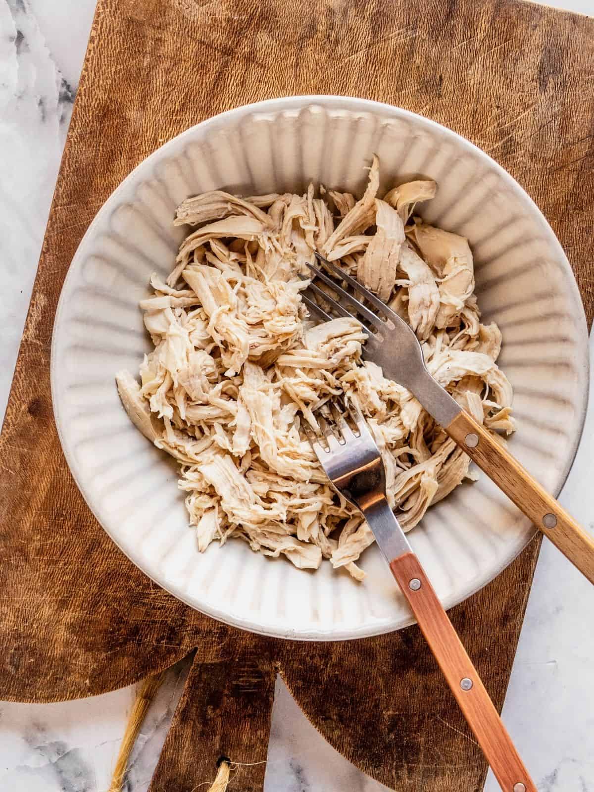 Recipe step showing the shredding of the chicken breast in a bowl with 2 forks.