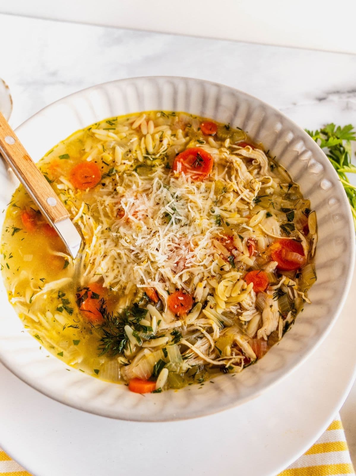 Lemon chicken orzo soup garnished with herbs and parmesan cheese in a bowl.
