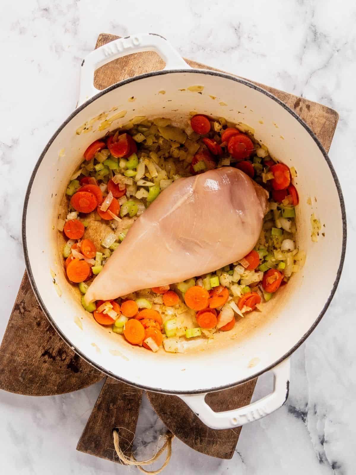 Recipe step showing the addition of the chicken breast to the soup pot with the aromatics.