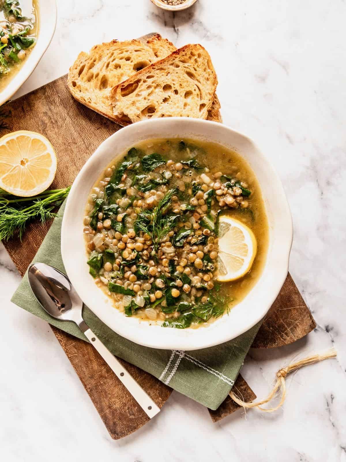 Lentil soup with Swiss chard and lemon garnished with dill and a lemon wedge in a bowl.
