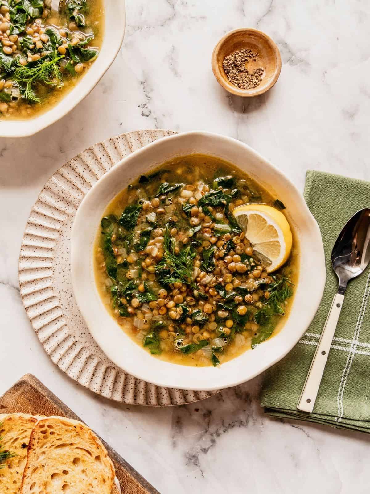 Swiss chard and Lentil soup with lemon garnished with dill and a lemon wedge in a bowl.