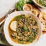 Lentil soup with Swiss chard and lemon garnished with dill and a lemon wedge in a bowl.
