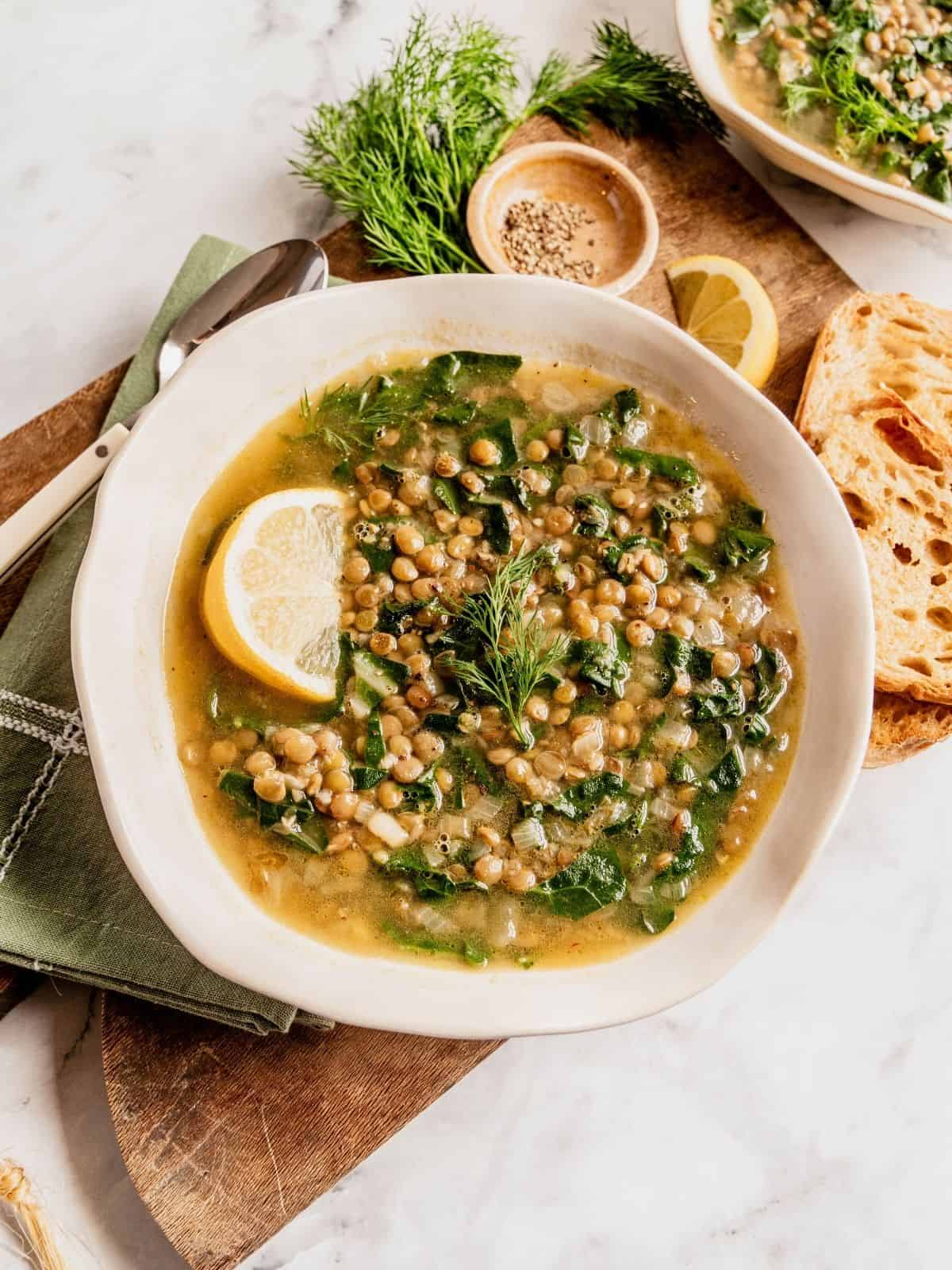 Lentil soup with Swiss chard and lemon garnished with dill and a lemon wedge in a bowl.