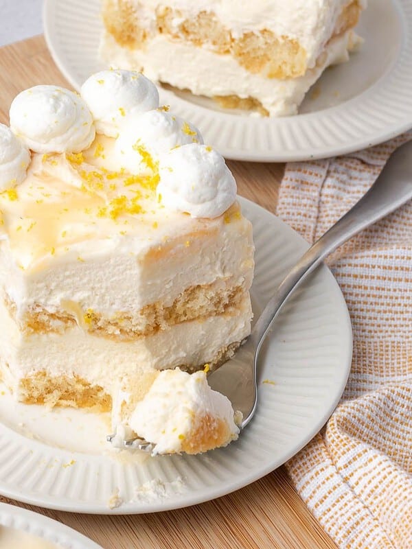 A slice of limoncello tiramisu decorated with whipped cream and lemon zest on a plate with a fork.