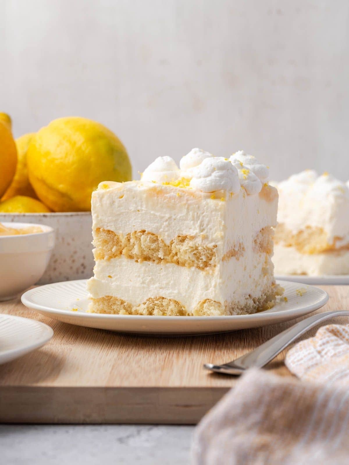 A slice of limoncello tiramisu decorated with whipped cream and lemon zest on a plate with a fork.