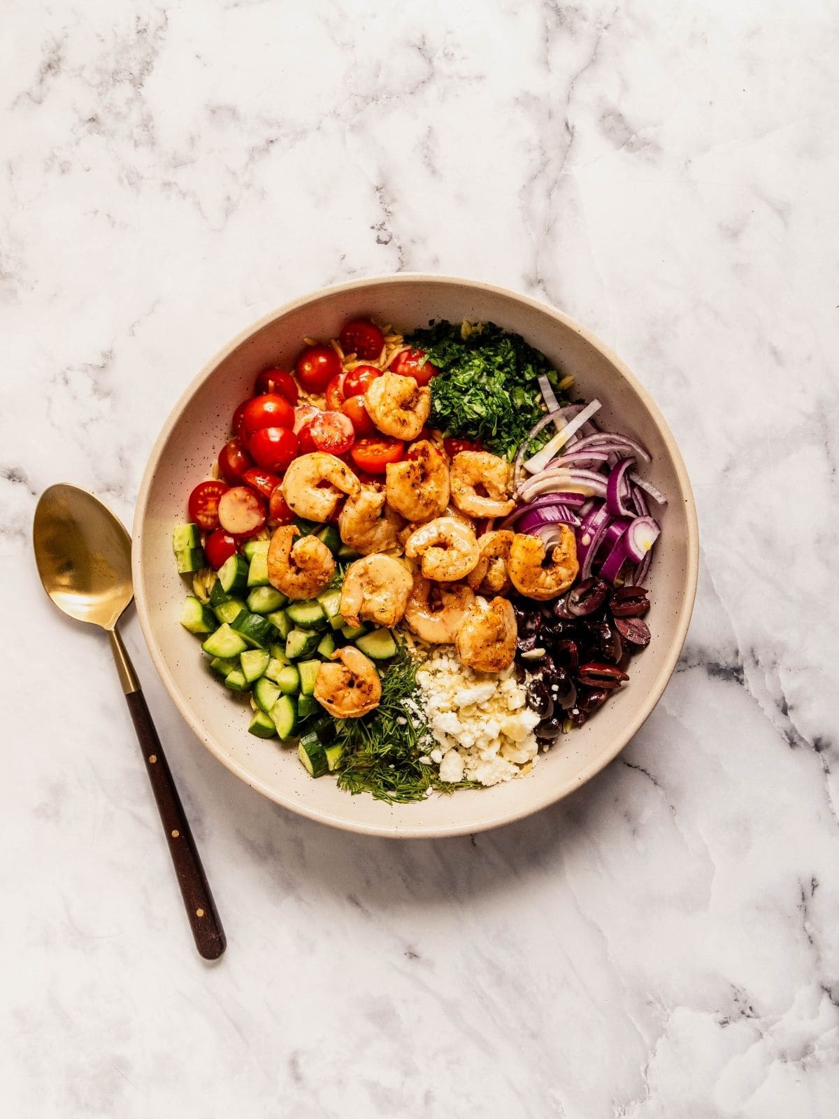Bowl with chopped tomatoes, cucumbers, herbs, olives, feta, onions and cooked shrimp.