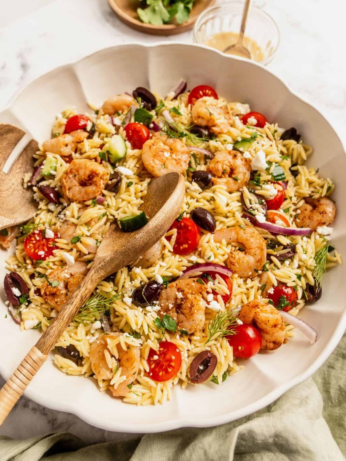 Mediterranean orzo salad with shrimp, olives, tomatoes, cucumbers and sliced onions in a bowl.
