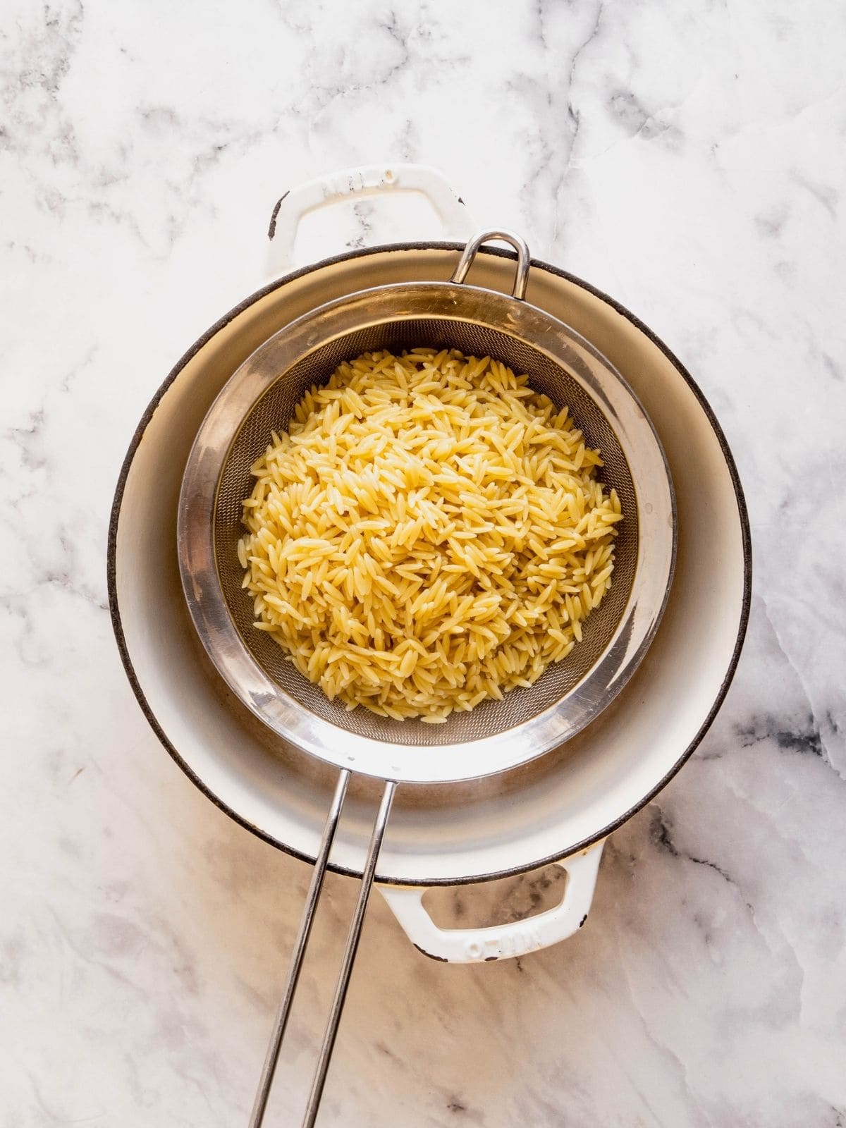 Cooked orzo draining in a sieve over a pot.