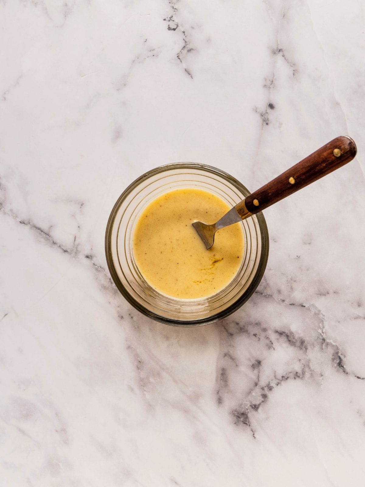 Salad dressing consisting of olive oil, lemon juice, mustard, and seasoning in a mall bowl.