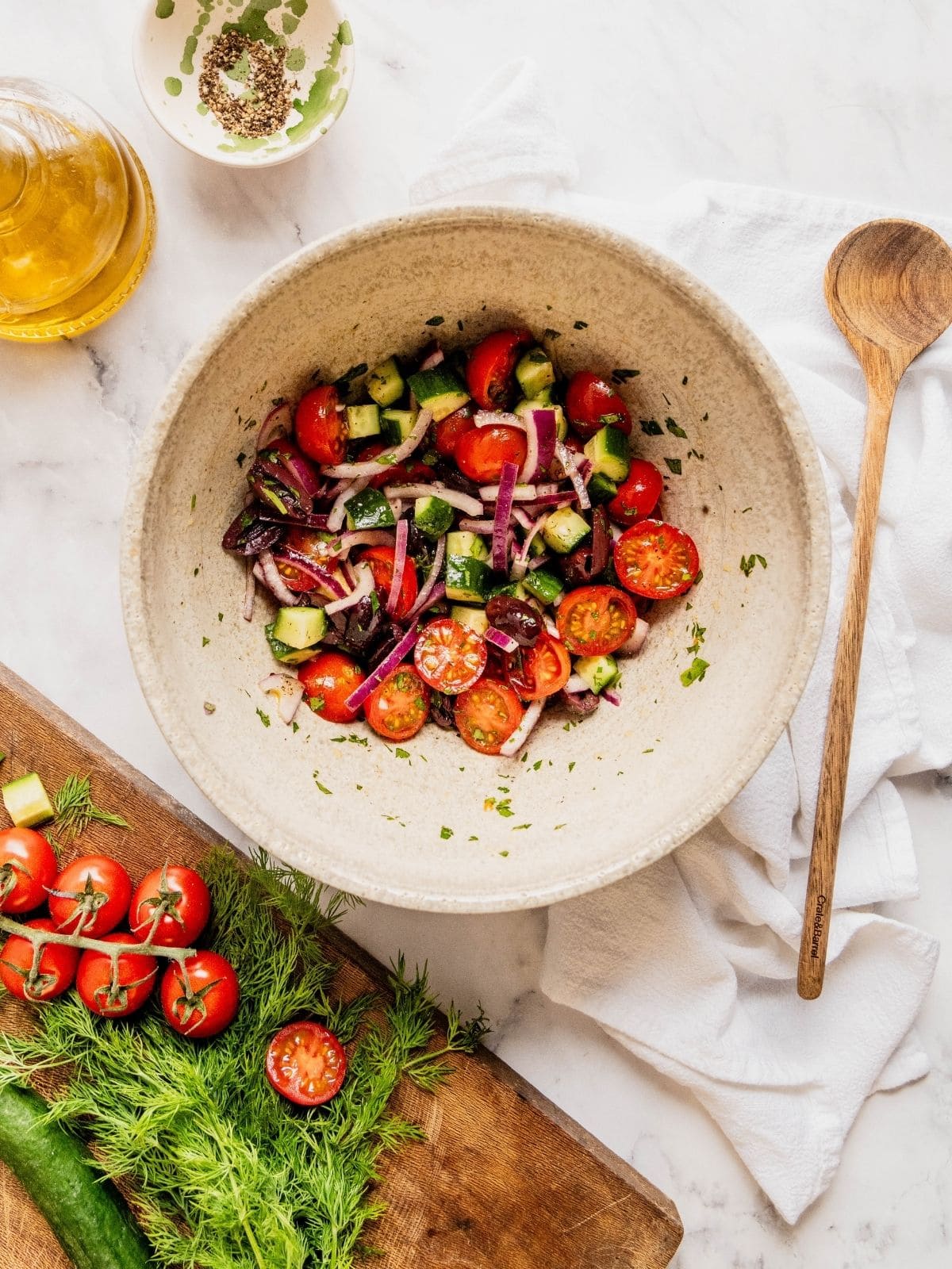 Bowl with chopped cucumbers, halved cherry tomatoes, sliced onions and olives.