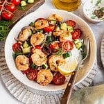 Mediterranean shrimp rice bowl with chopped cucumber, tomatoes, olives garnished with fresh dill.